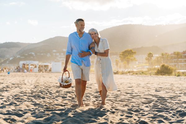 A couple walking together barefoot on the beach while holding a basket