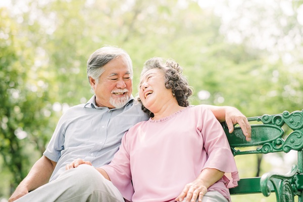 A senior couple sitting on a bench in the park and laughing.