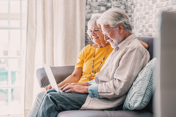 Senior couple sitting on a couch together doing some typing on a laptop