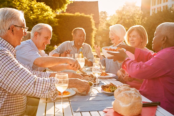 Six people sitting around a table outside passing food to one another