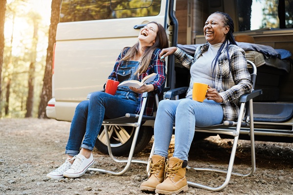 Two women sitting in lawn chairs outside a campervan in the forest